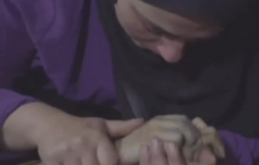 Thumbnail preview image for the video titled: Mother kisses the hands of her daughter killed in the Israeli bombing of Abu Hamisa school